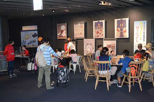 大勢の親子連れでにぎわうKCG協力の「描いて撮って！ お絵描きワークショップ」。京都国立博物館に展示している文化財を表現した大型モザイクアート作品も展示されています＝2017年7月8日，京都水族館「交流プラザ」