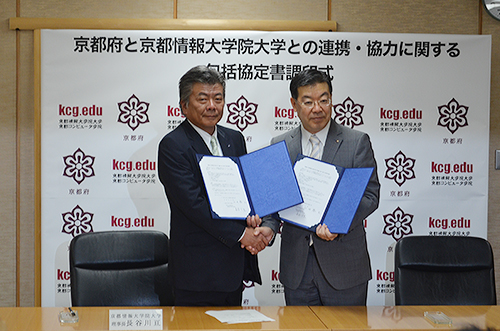 KCGIと京都府との連携・協力に関する包括協定書にサインし握手を交わす長谷川亘理事長(左)と山田啓二 京都府知事=2015年5月26日,京都府庁