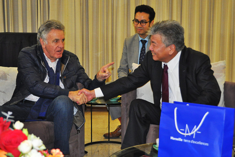 今後の提携に向け，握手を交わすロアッタ副市長と長谷川統括理事長